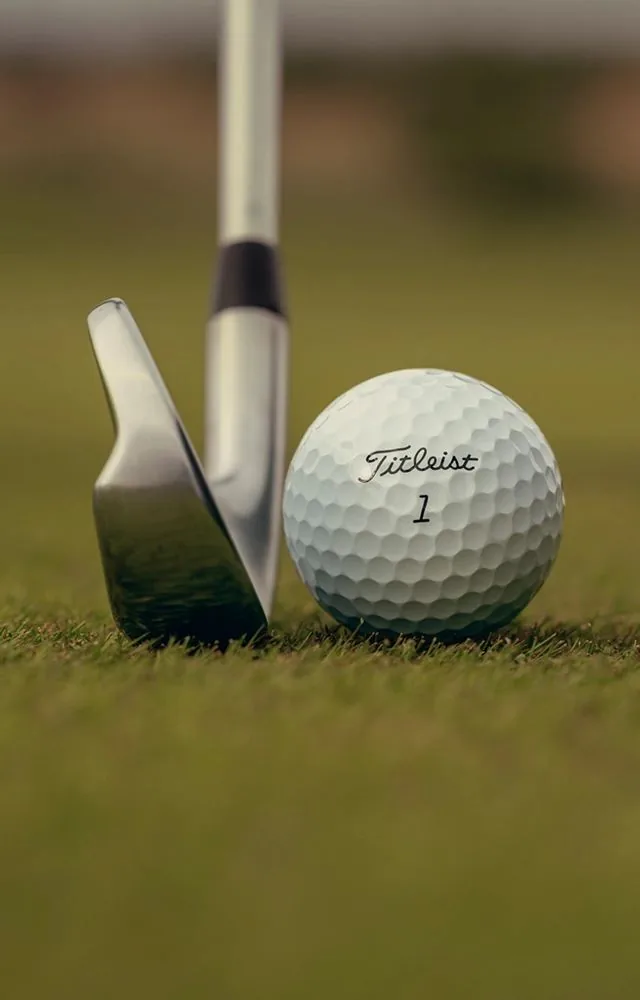 A close-up golf ball beside an iron club, representing Loft Golfing contact and event enquiries.
